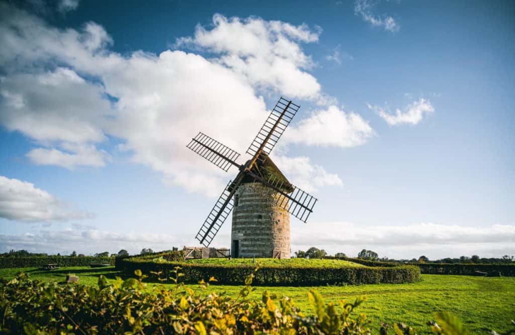 Moulin à vent traditionnel contre un ciel partiellement nuageux avec verdure environnante.