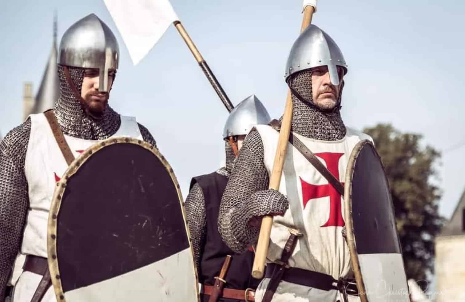 Des reconstituteurs habillés en chevaliers médiévaux en armure, portant des boucliers et un drapeau.
