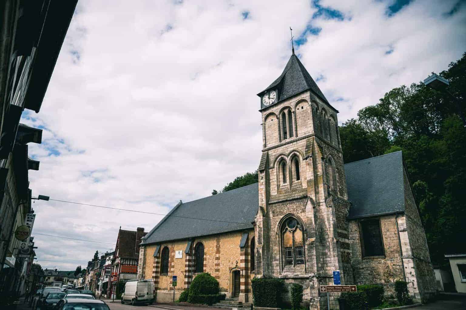 Une église historique en pierre avec une tour d'horloge, située le long d'une rue d'une ville européenne.