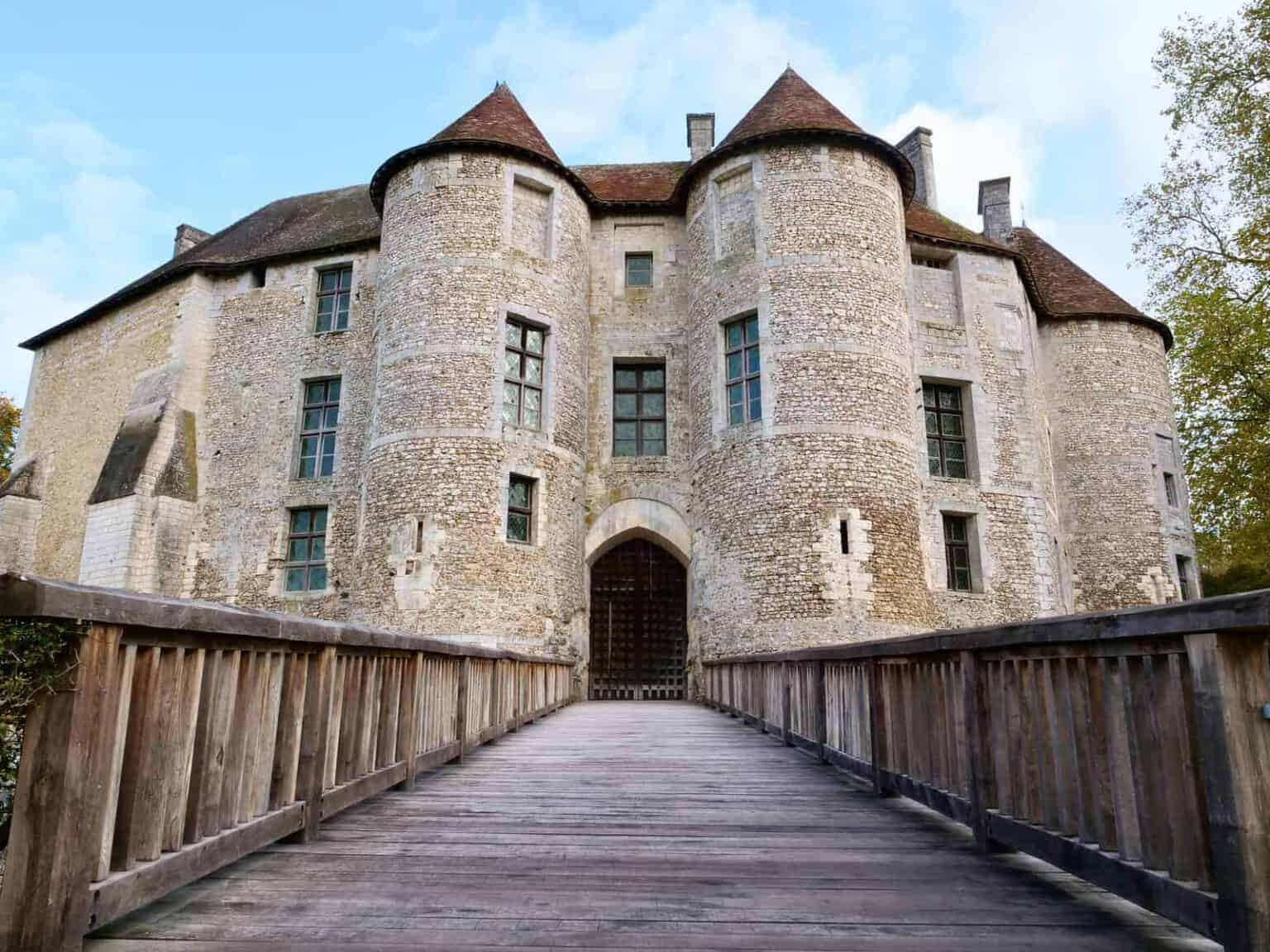 Château médiéval en pierre avec tours accessible par un pont en bois.