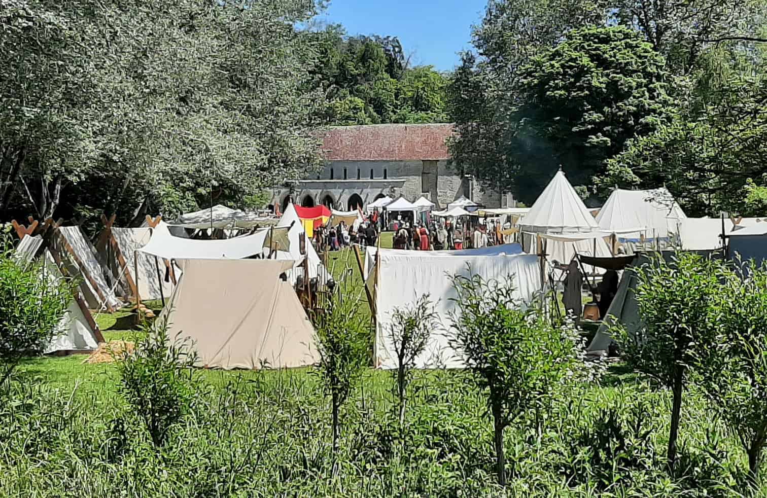 Foire médiévale avec chapiteaux et reconstituteurs dans un cadre extérieur ensoleillé.