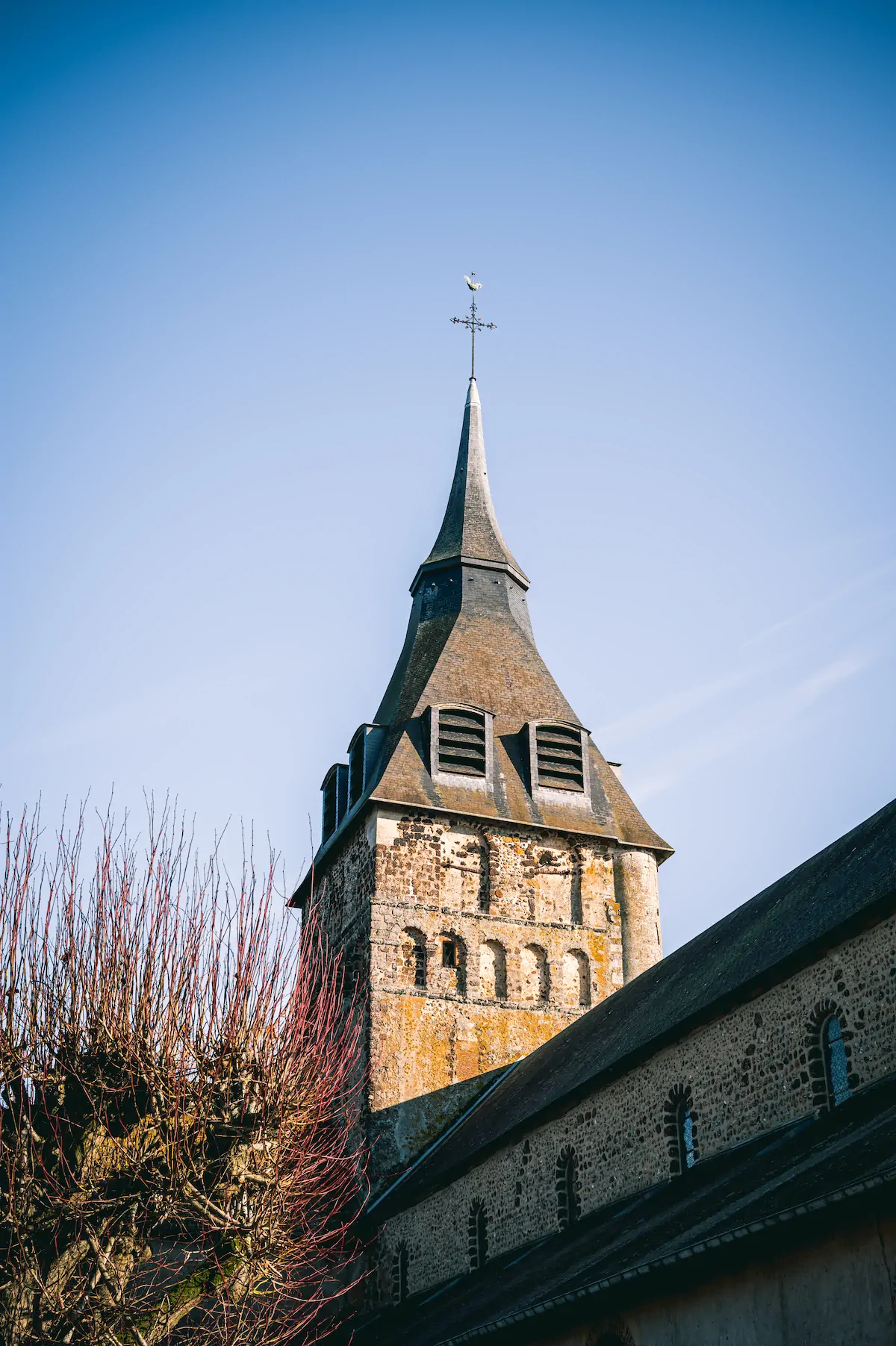 Clocher de l'église en pierre avec une flèche contre un ciel bleu clair.